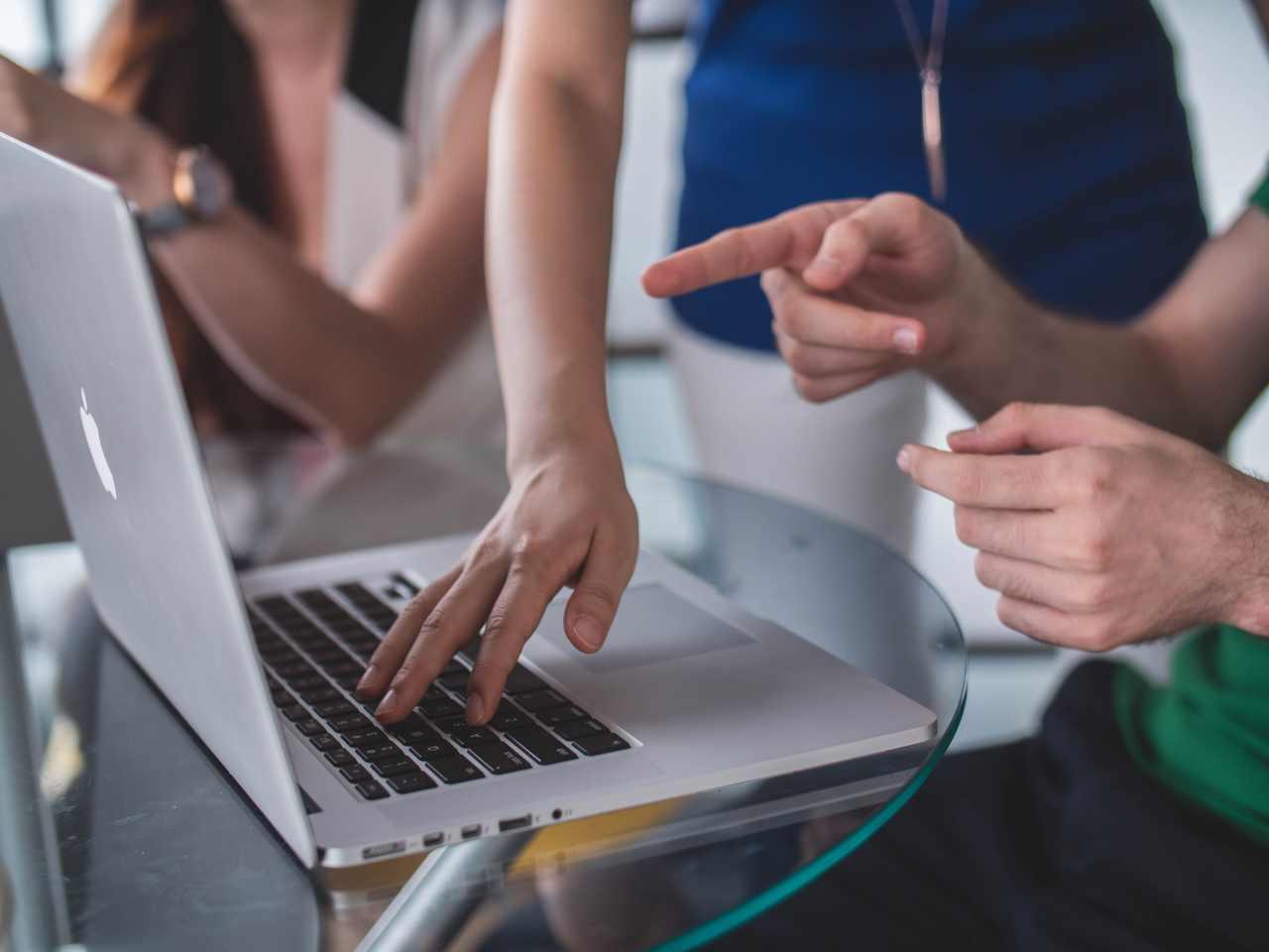 Grupa ludzi wskazujących placem w stronę włączonego laptopa.