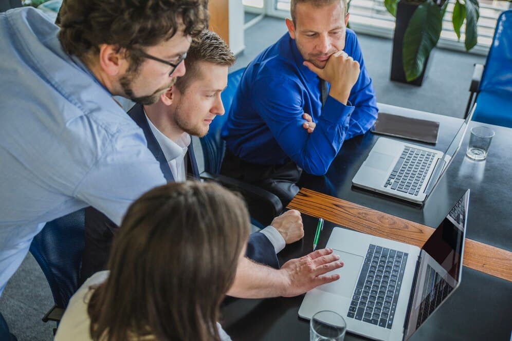 A group of discussing employees in the office, focused over a laptop, indicating joint problem solving