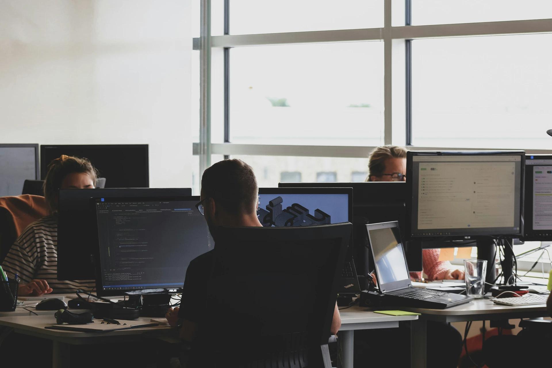 Team of programmers working at computers in an office with an outdoor view.