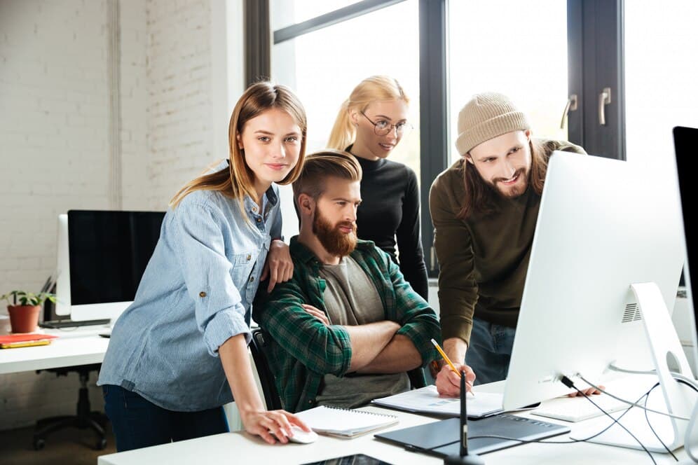 A group of young people in an office, gathered around a computer, working together on a project, suggesting intense collaboration and a creative atmosphere.