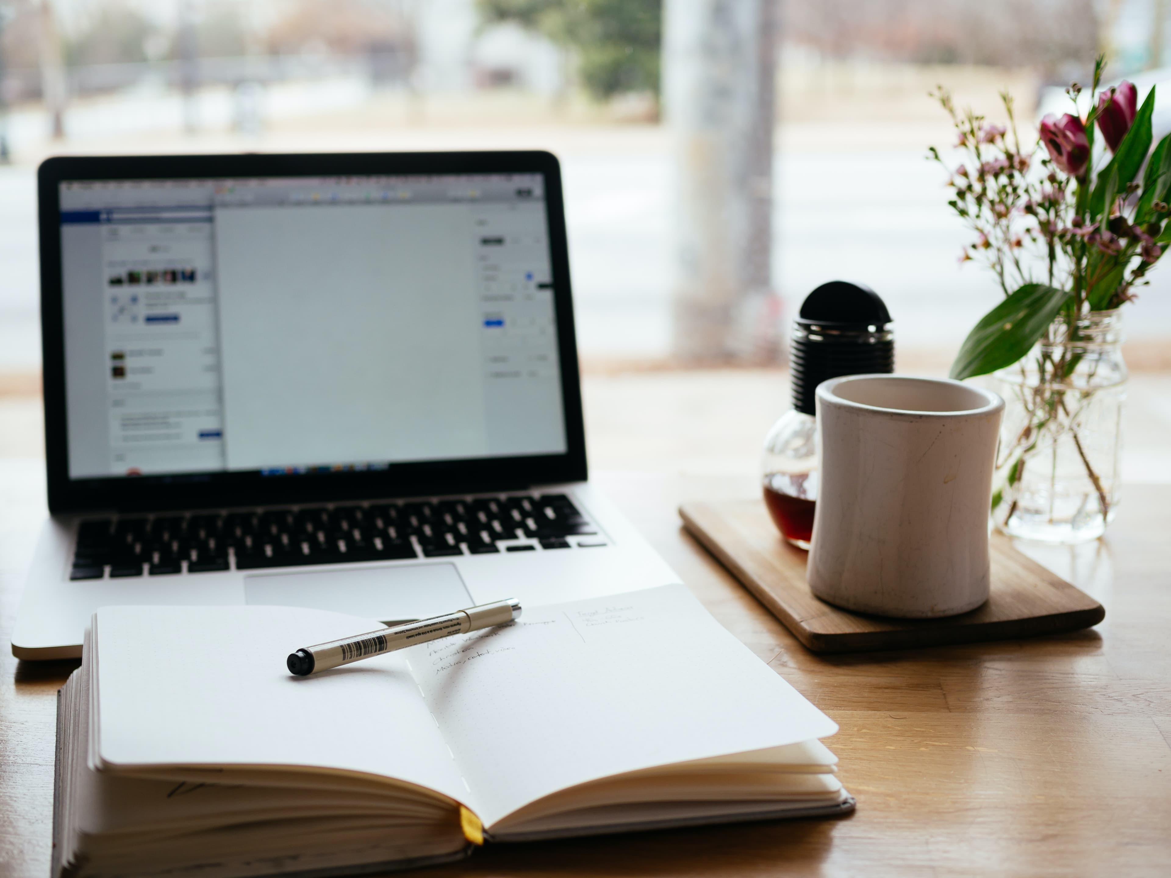 A desk with a laptop, notebook, and a cup of coffee in a cozy setting.