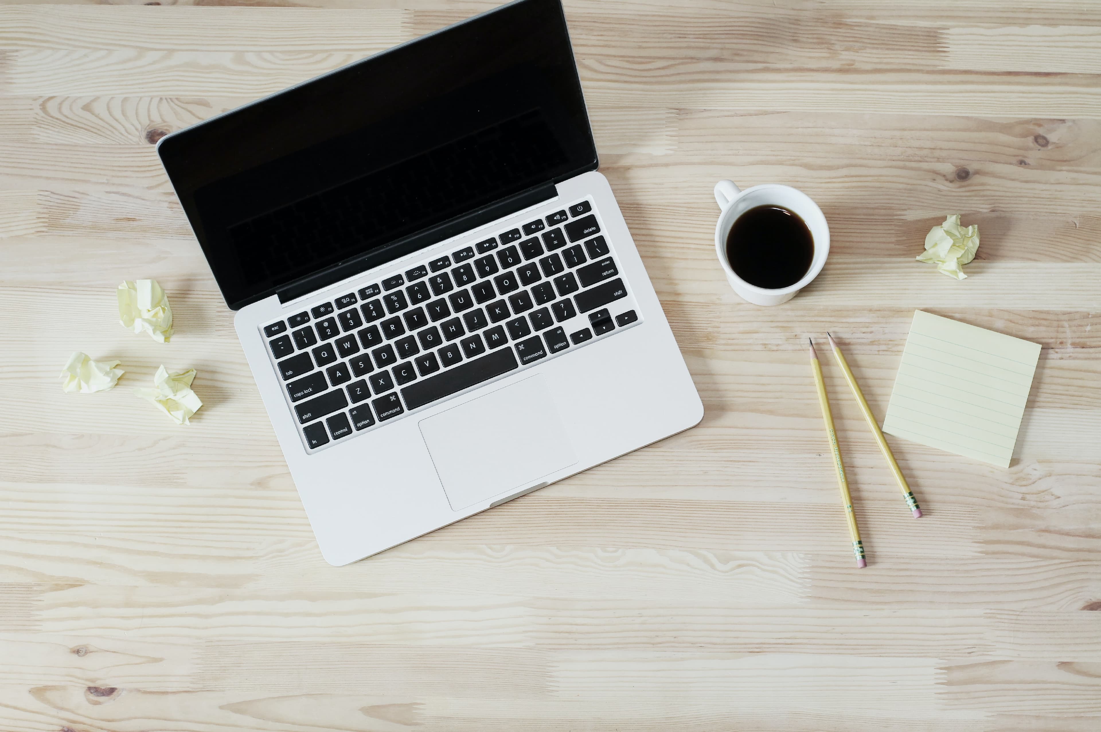 Top view of a desk with a laptop, cup of coffee, pencils, and sticky notes