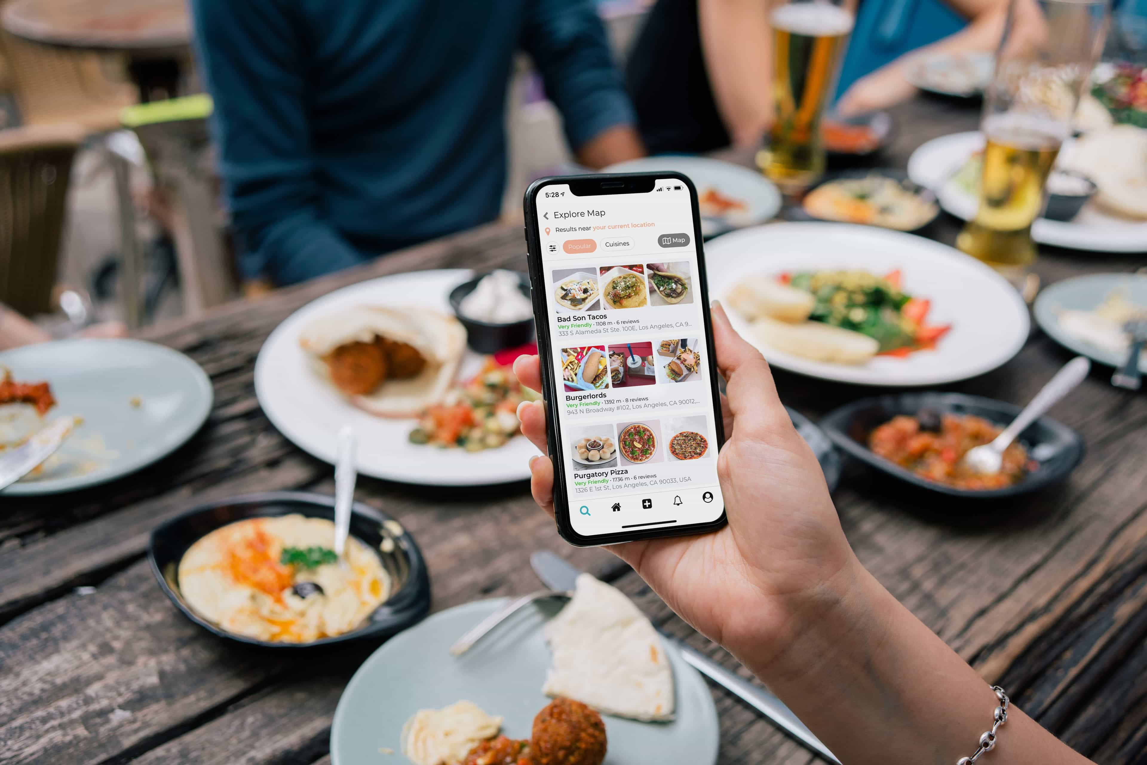 Osoba przeglądająca menu restauracji na smartfonie przy stole z jedzeniem.